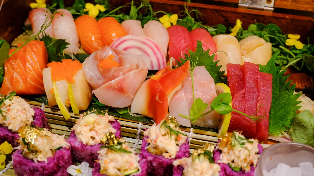 A wooden box of sashimi and sushi with edible flowers